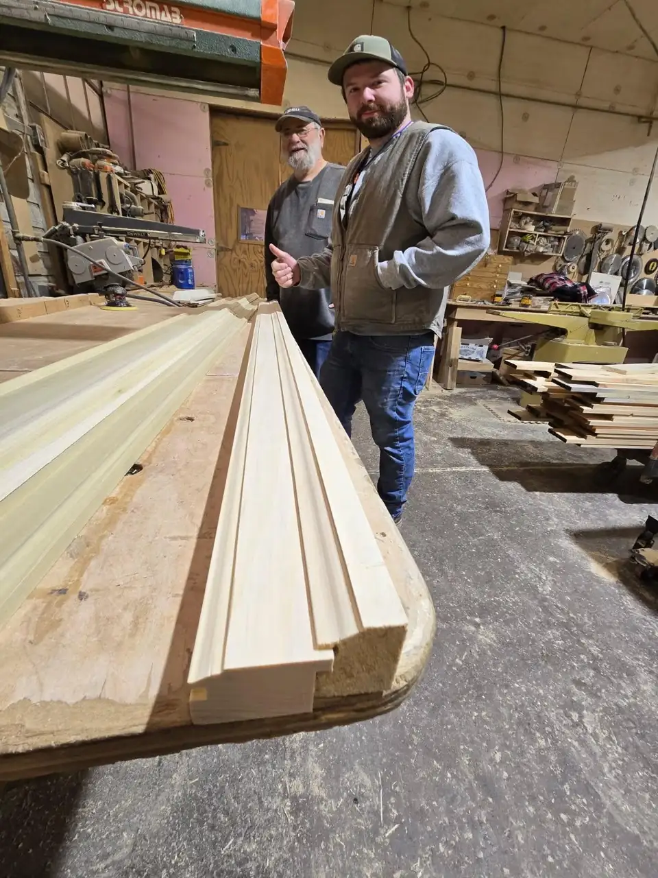 Custom millwork in Altoona: freshly milled hardwood mouldings on a bench in the Modern Cabinet & Construction woodshop, with two of the crew behind